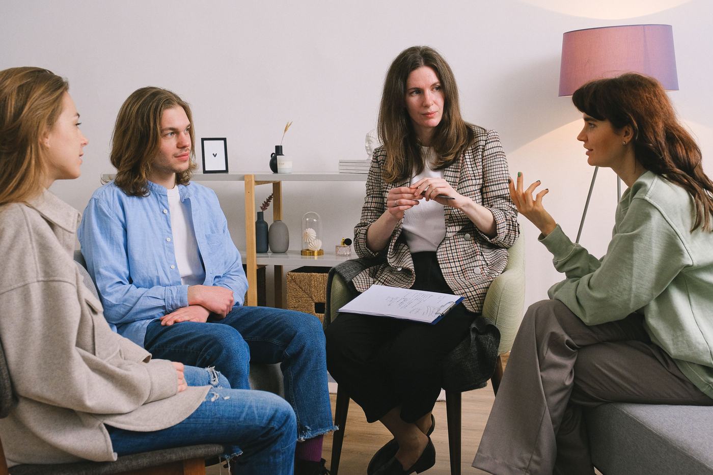 A clinician leading a group therapy session with three participants seated in a circle, one mid-sentence